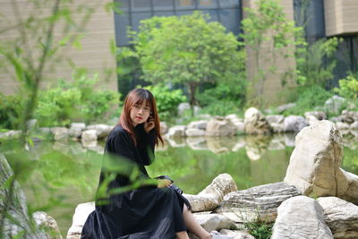 Portrait of teenage girl sitting on rock by lake