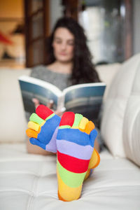 Woman with colorful socks while reading book on couch at home