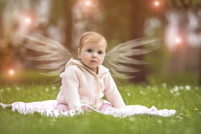 Cute baby girl with angel costume sitting on field