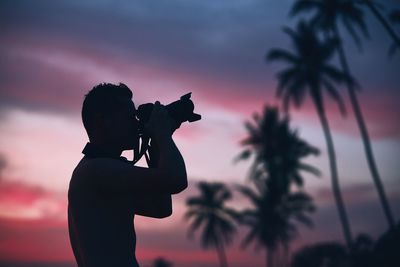 Silhouette man photographing against sky during sunset