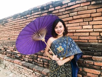 Portrait of young woman holding umbrella standing against brick wall