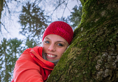 Portrait of smiling young woman against tree trunk in winter