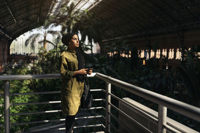 Portrait of young woman standing by railing