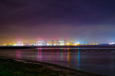 Illuminated city by river against sky at night