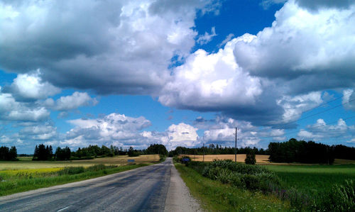 Road passing through field against cloudy sky