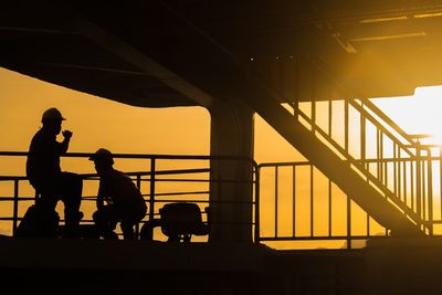 Silhouette workers below bridge during sunset