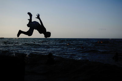 Silhouette boy jumping mid-air on beach