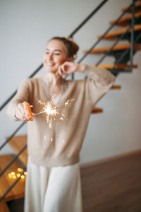 Smiling young woman holding sparkler at home