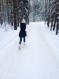 Rear view of woman walking on snow covered road amidst trees