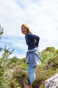 Side view portrait of cheerful young woman standing against sky