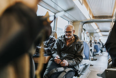 Elderly man using smart phone and sitting in bus while traveling to work