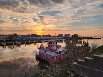 Buildings by river against sky during sunset