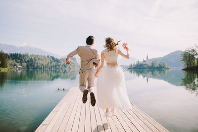 Rear view of couple jumping on pier over lake