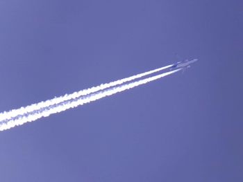 Low angle view of vapor trails against clear blue sky