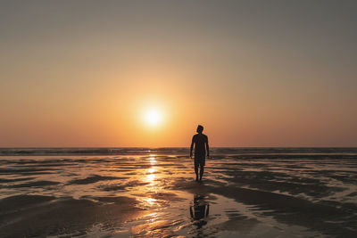 Silhouette man walking at beach against sky during sunset