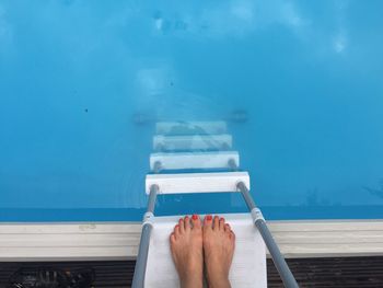 Low section of woman standing on ladder at swimming pool