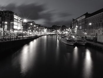 Boats moored in river against illuminated city at night