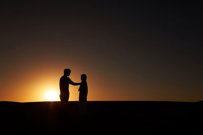 Silhouette man and woman standing against sky during sunset