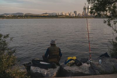 Rear view of men sitting by river against sky