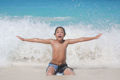 Portrait of shirtless man with arms raised in sea