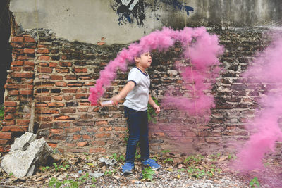 Boy playing with distress flare while standing against brick wall