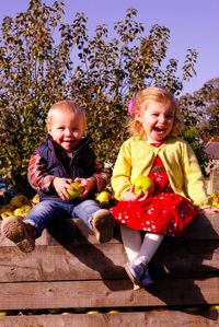 Portrait of smiling siblings with fruits sitting at orchard