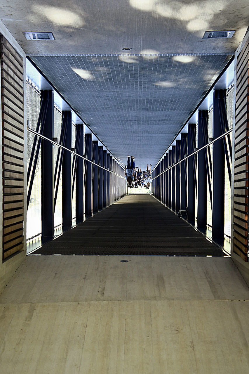 PEOPLE WALKING ON FOOTBRIDGE WITH CEILING IN EMPTY CORRIDOR