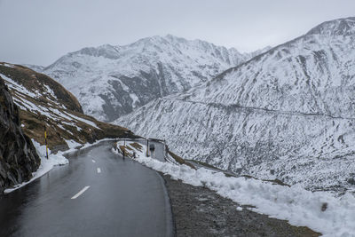 Pass road in the alps lined with snow-covered mountains and a car in the background.