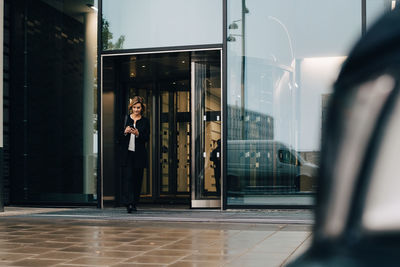 Full length of businesswoman using smart phone while leaving from office