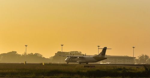 Airplane on airport runway against sky during sunset