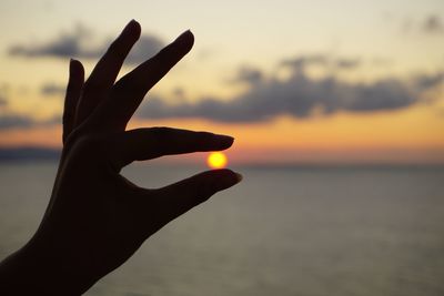 Optical illusion of silhouette hand holding sun over sea against sky during sunset