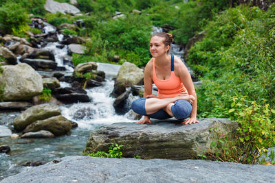 Full length of woman sitting on rock by plants