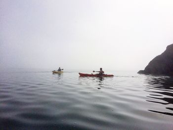 People kayaking in sea against clear sky