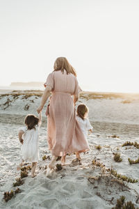 Behind view of mother walking with toddler girl twins to ocean