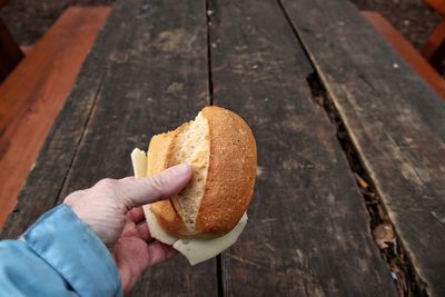 Human hand holding bread against wooden table 