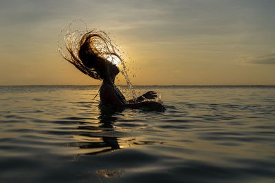 View of swimming in sea against sunset sky