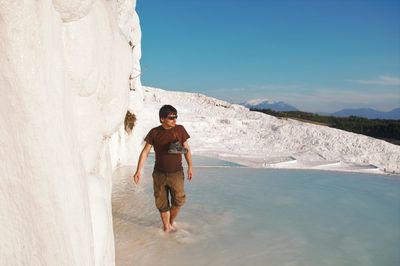 Full length of young man standing on rock against sky