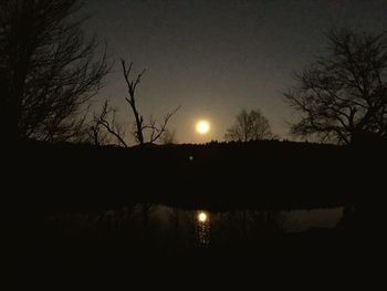 Silhouette bare tree by lake against sky at night