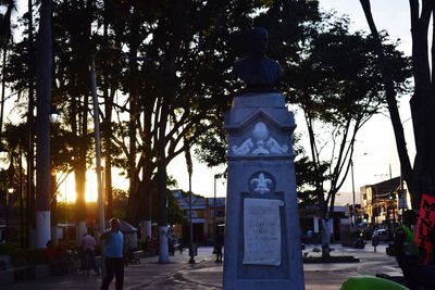 Statue in city against sky at sunset