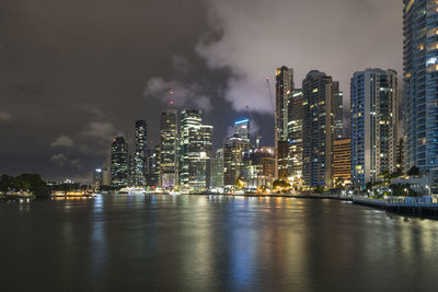 Illuminated city by sea against sky at night