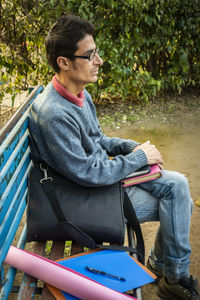 Side view of young man sitting on bench