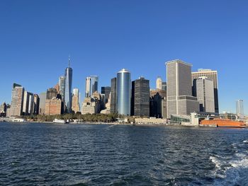 Buildings by river against clear blue sky