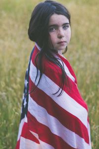 Portrait of girl wrapped in american flag while standing on field