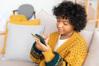 Young woman using mobile phone while sitting on bed at home