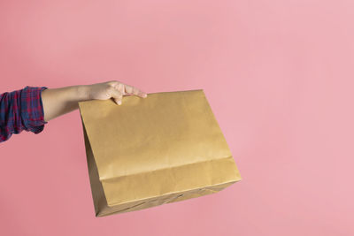 Close-up of hand holding umbrella against pink background