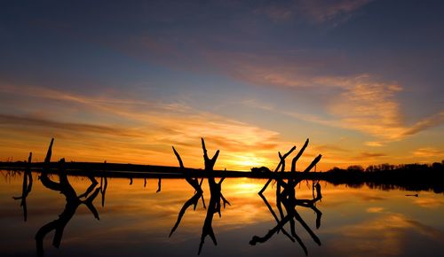 Silhouette wooden posts in lake against sky during sunset