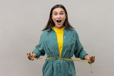 Surprise woman with tape measure against gray background