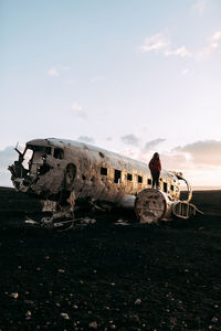Young tourist standing on wrecked aircraft between deserted lands and blue sky