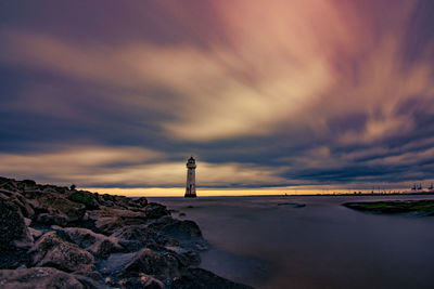 Lighthouse by sea against sky during sunset