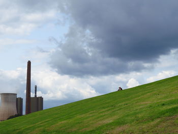 Low angle view of friends sitting on hill by cooling tower against cloudy sky